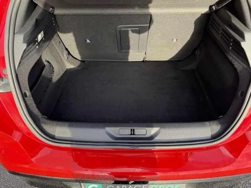 Coffre ouvert vu de dessus d’une Peugeot 308 2024 Rouge Elixir, montrant l’espace de rangement vide et les finitions intérieures noires.