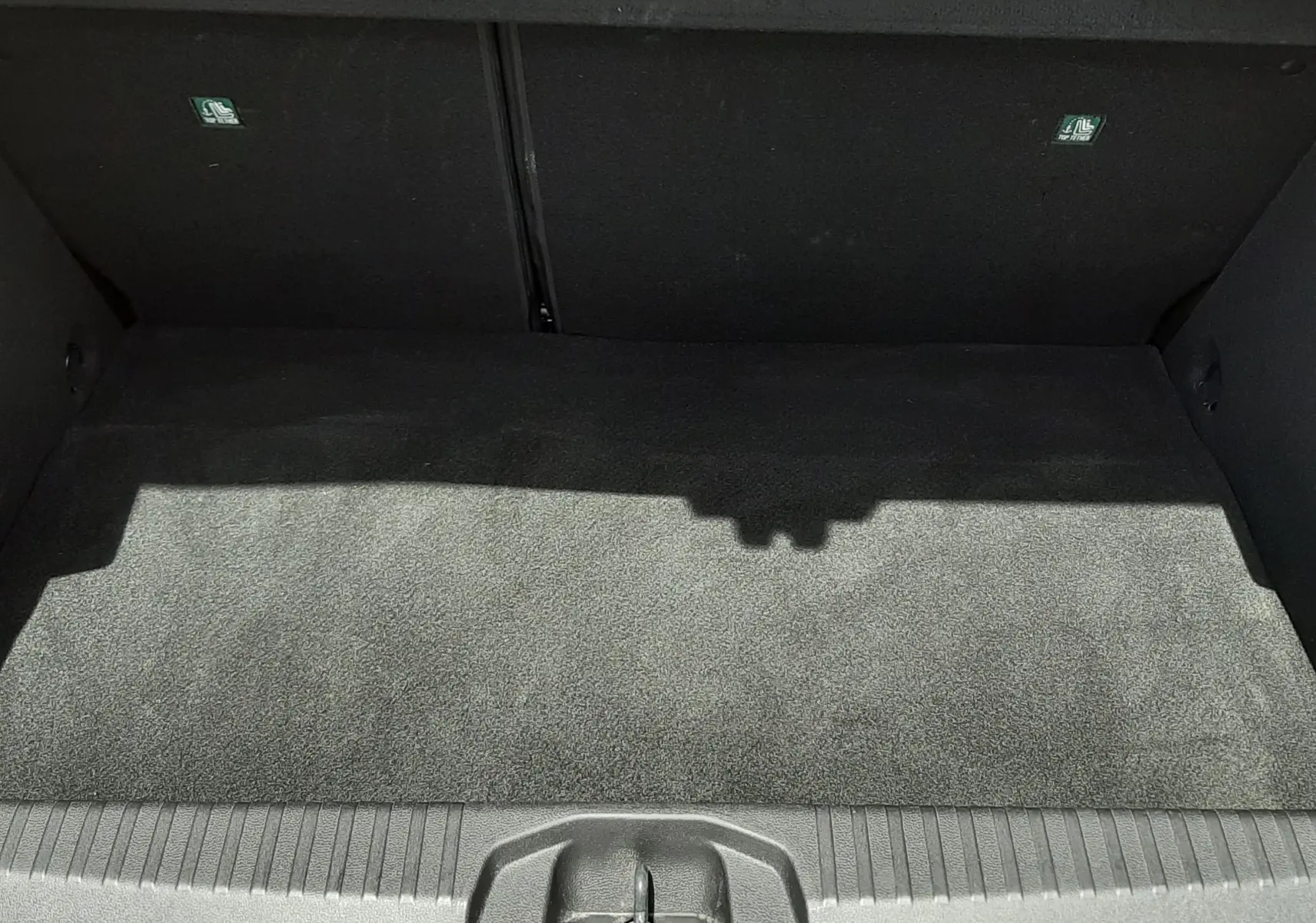 Coffre ouvert vu de face d’une Renault Clio V rouge flamme métal, montrant un espace de chargement propre et vide.