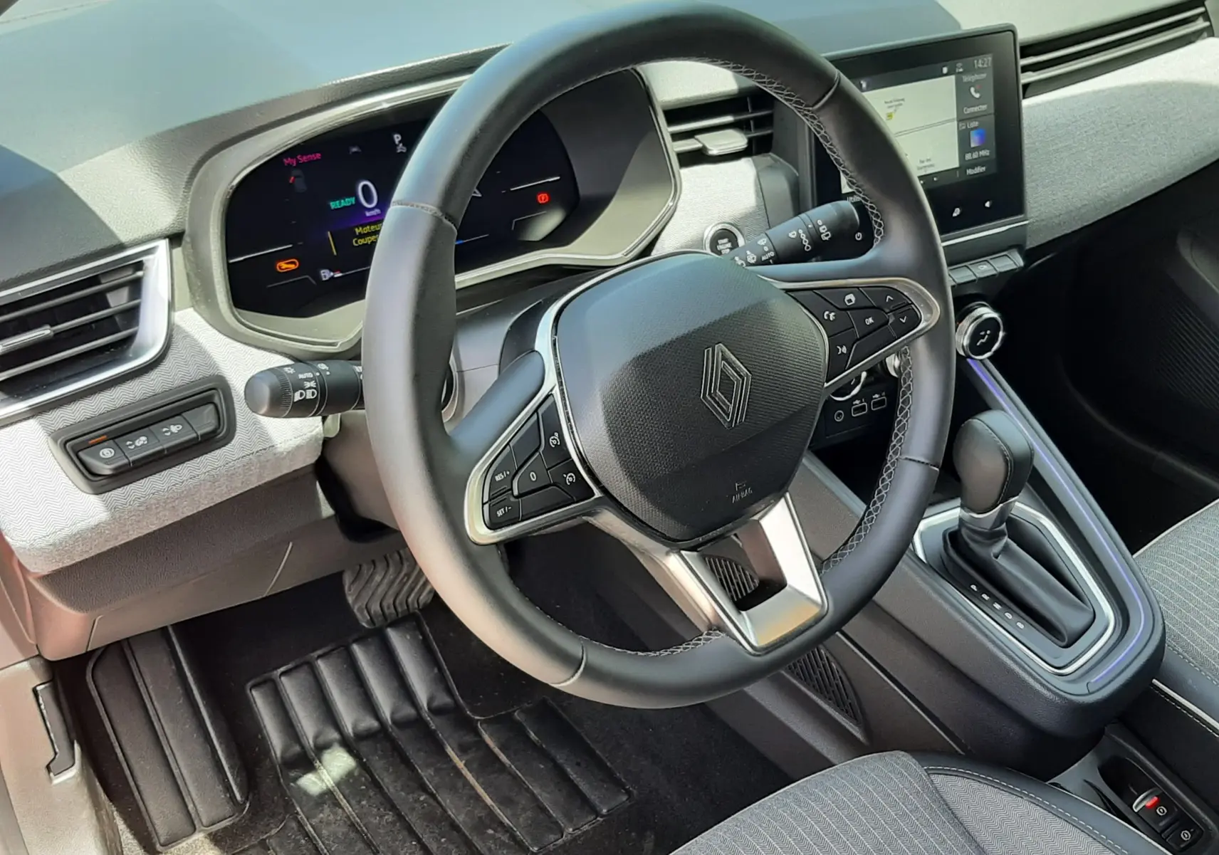 Vue intérieure du poste de conduite de la Renault Clio V rouge flamme, avec volant multifonction et écran tactile central.