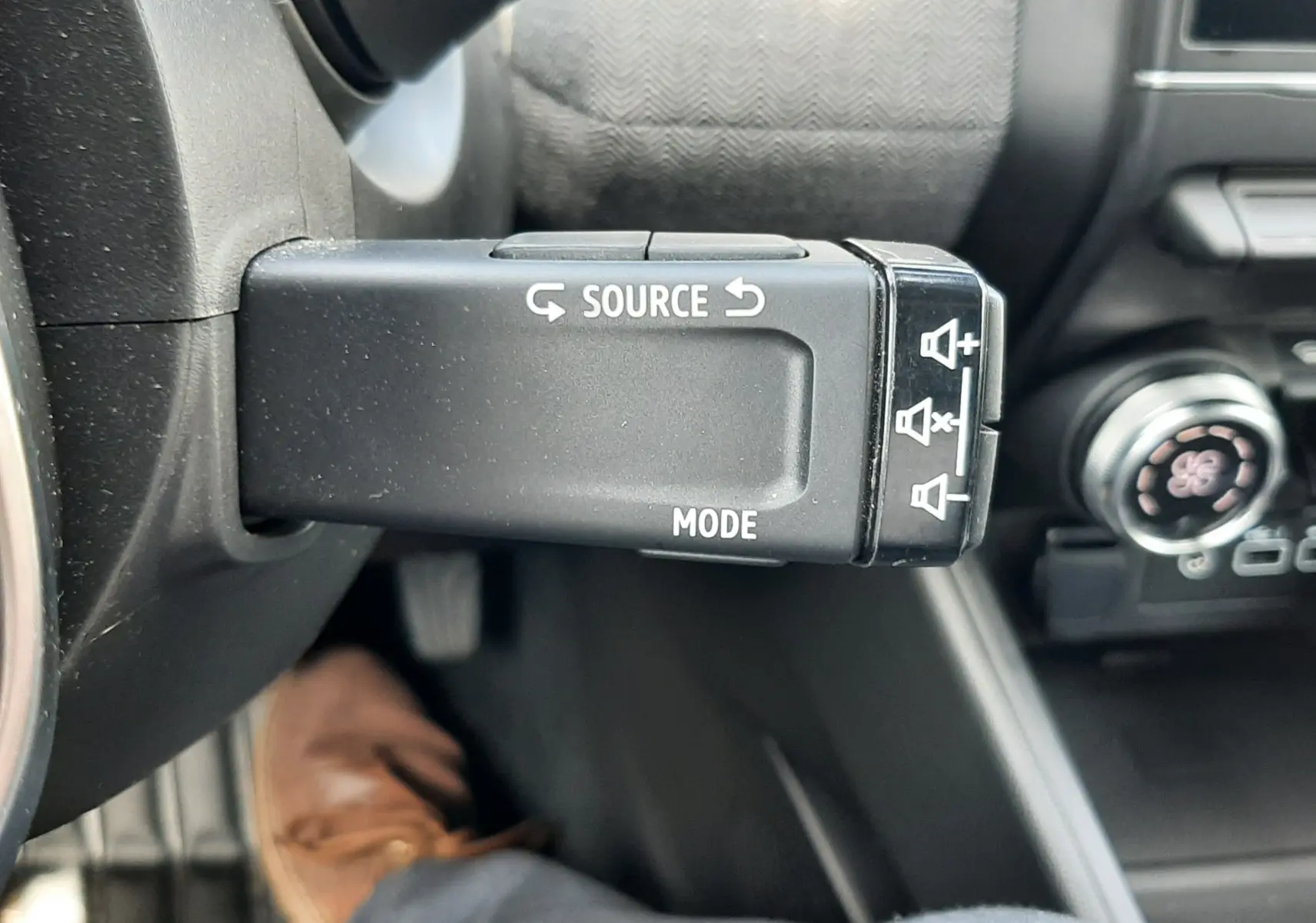 Gros plan sur la commande multimédia au volant côté gauche de la Renault Clio V rouge flamme, intérieur gris noir.