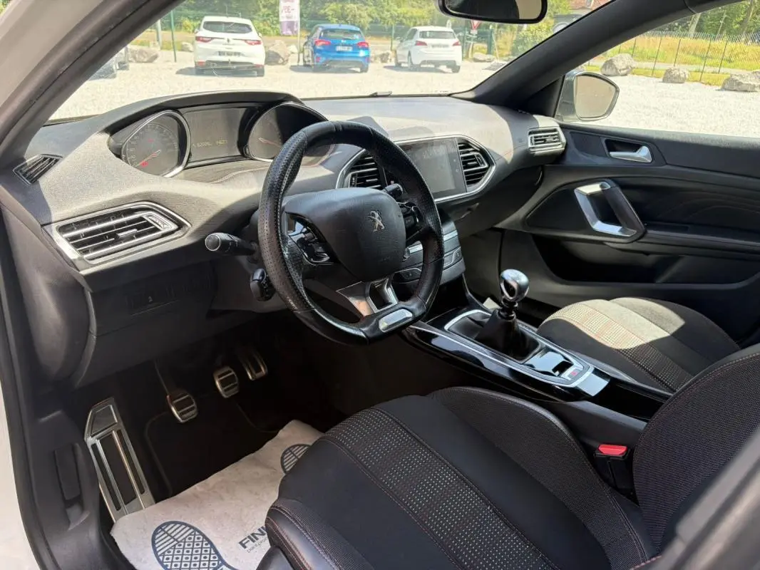 Vue intérieure côté conducteur de la Peugeot 308 GT-Line 2017, avec volant cuir, levier de vitesses manuel et sièges noirs.