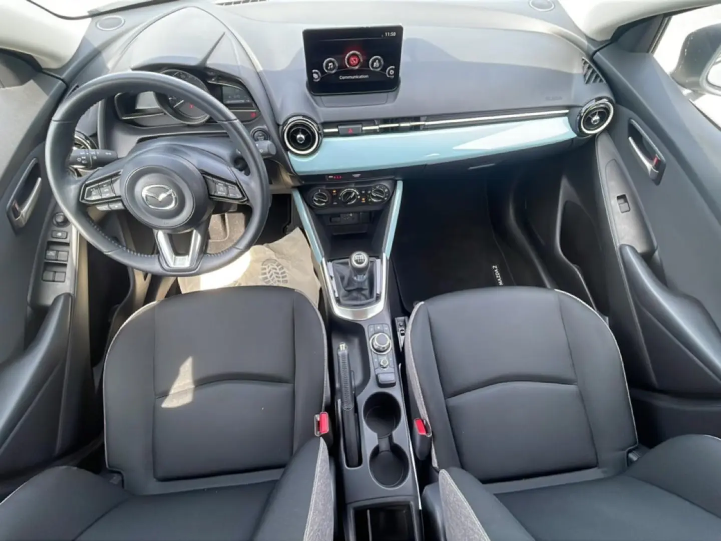 Vue intérieure de la Mazda2 2024 montrant le tableau de bord, volant cuir multifonction et levier de vitesse manuel.