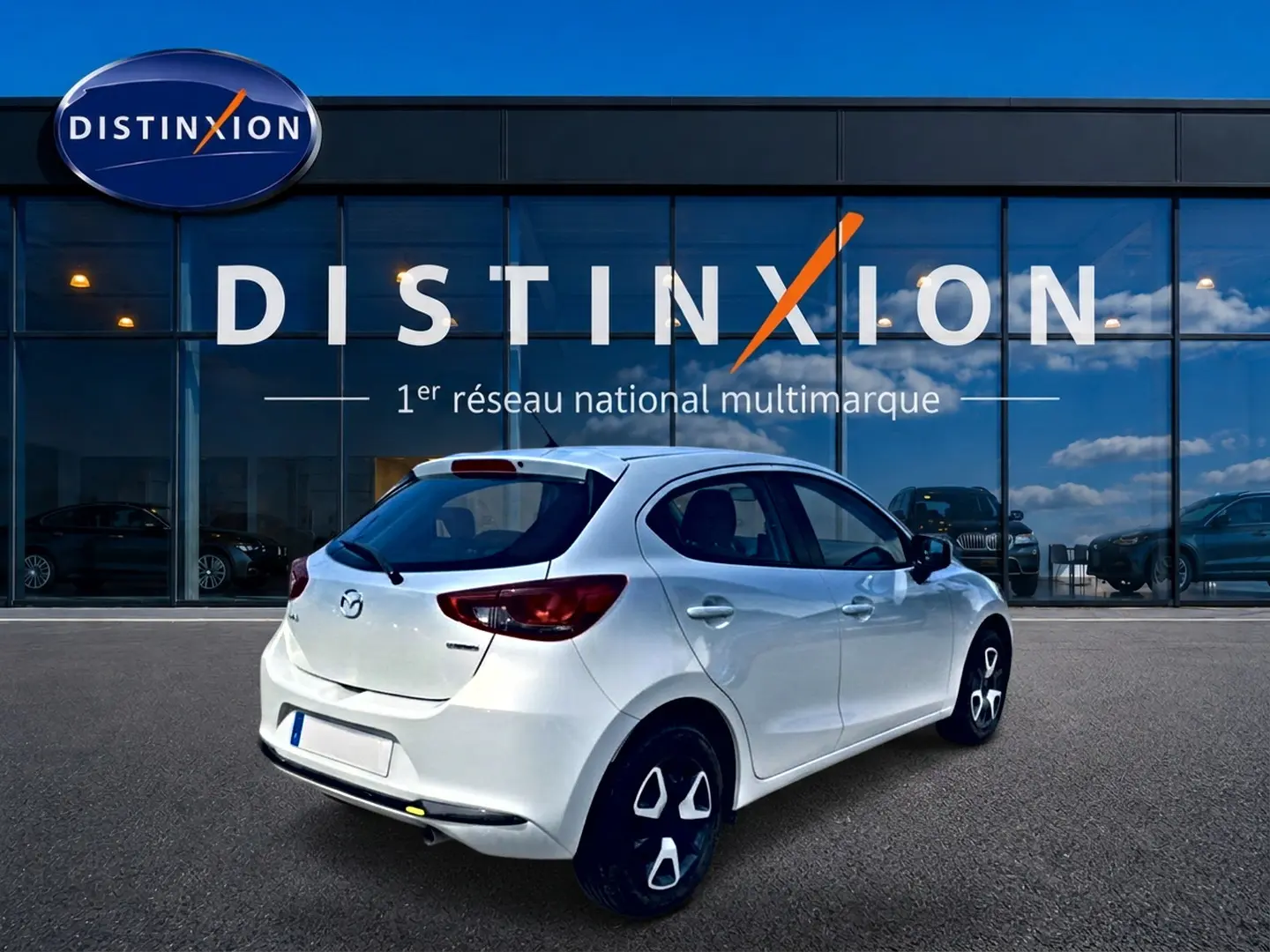 Vue 3/4 arrière droite d'une Mazda2 blanche 2024 stationnée devant une vitrine Distinxion.