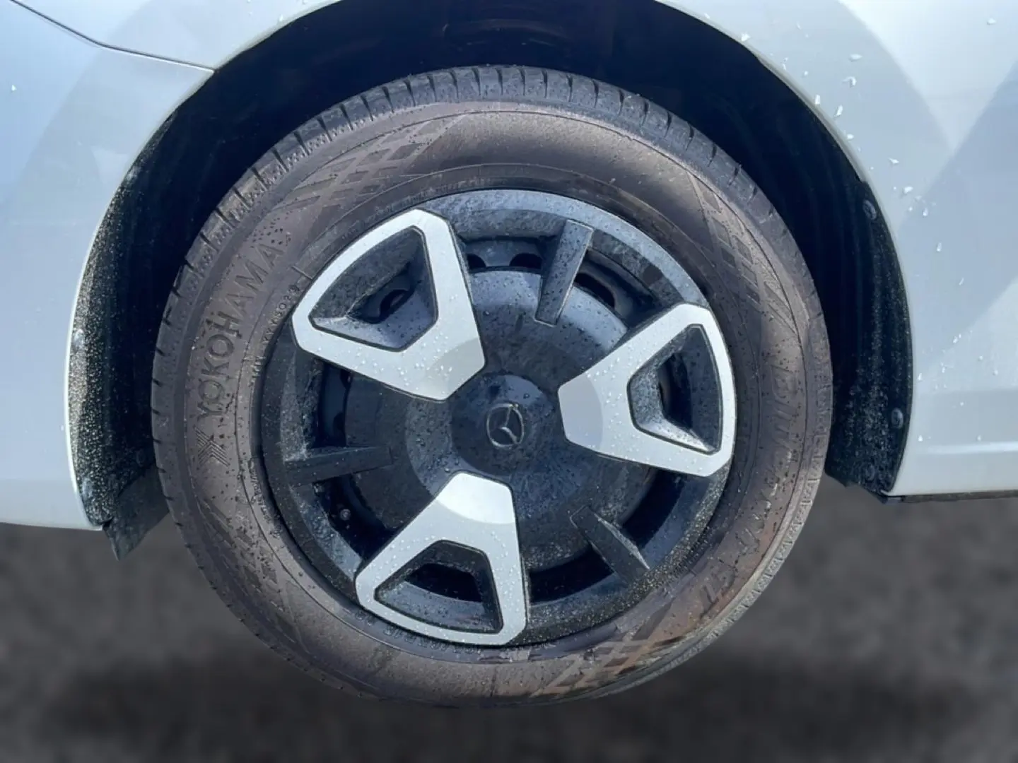 Gros plan sur la roue avant droite d'une Mazda2 blanche avec enjoliveur noir et argenté au design triangulaire.