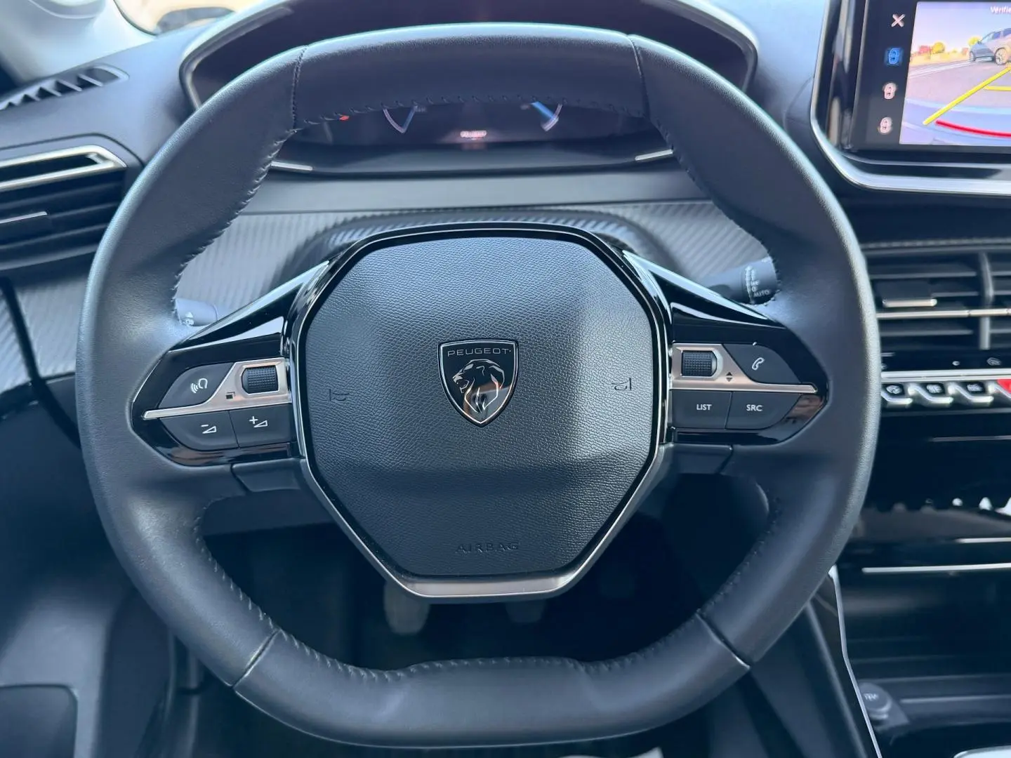 Vue rapprochée du volant cuir noir du Peugeot 208 2025 avec commandes intégrées et tableau de bord numérique partiel.