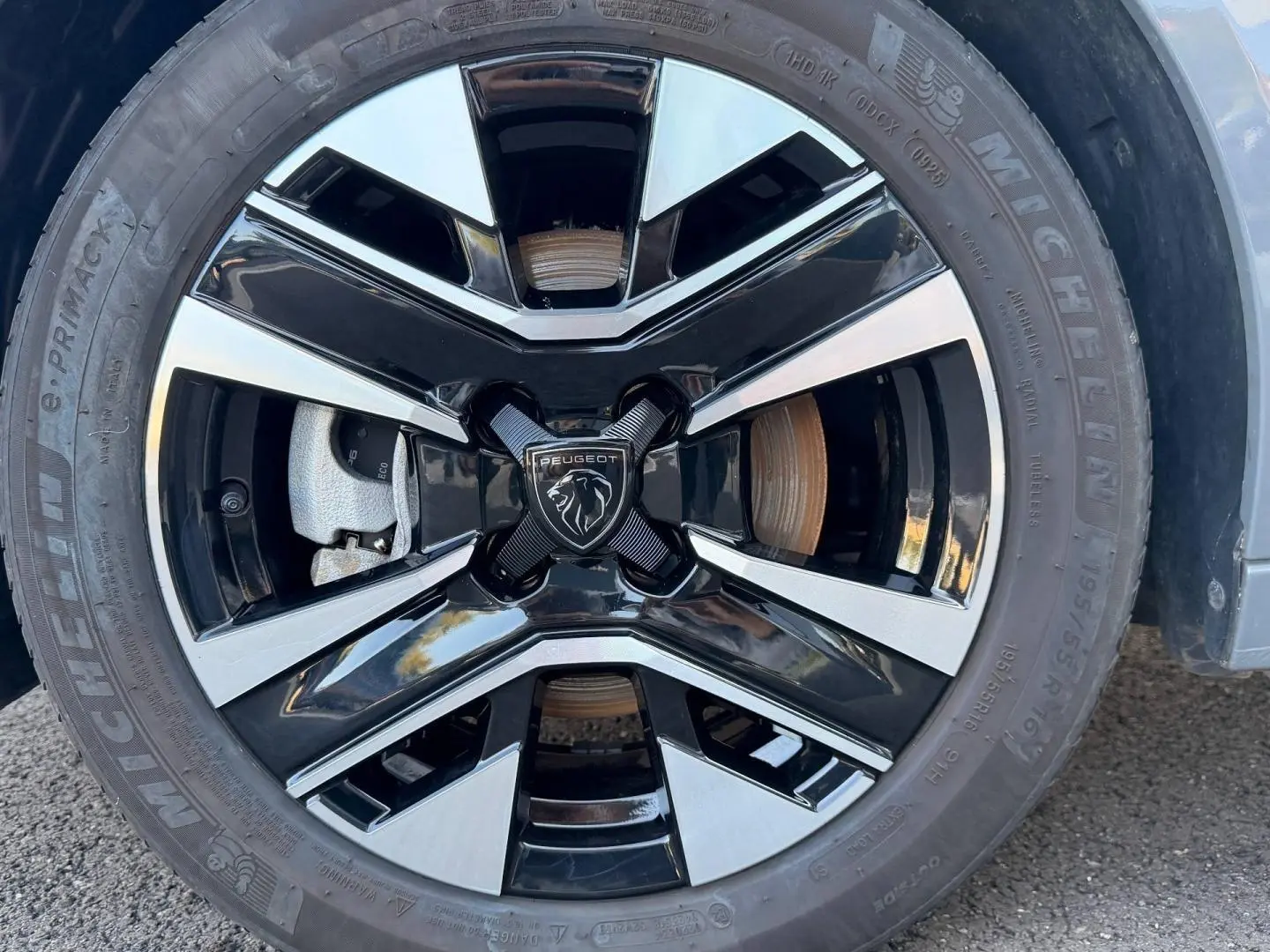 Gros plan sur la jante alu bicolore noire et argentée d'une Peugeot 208 Gris Artense avec logo lion central.