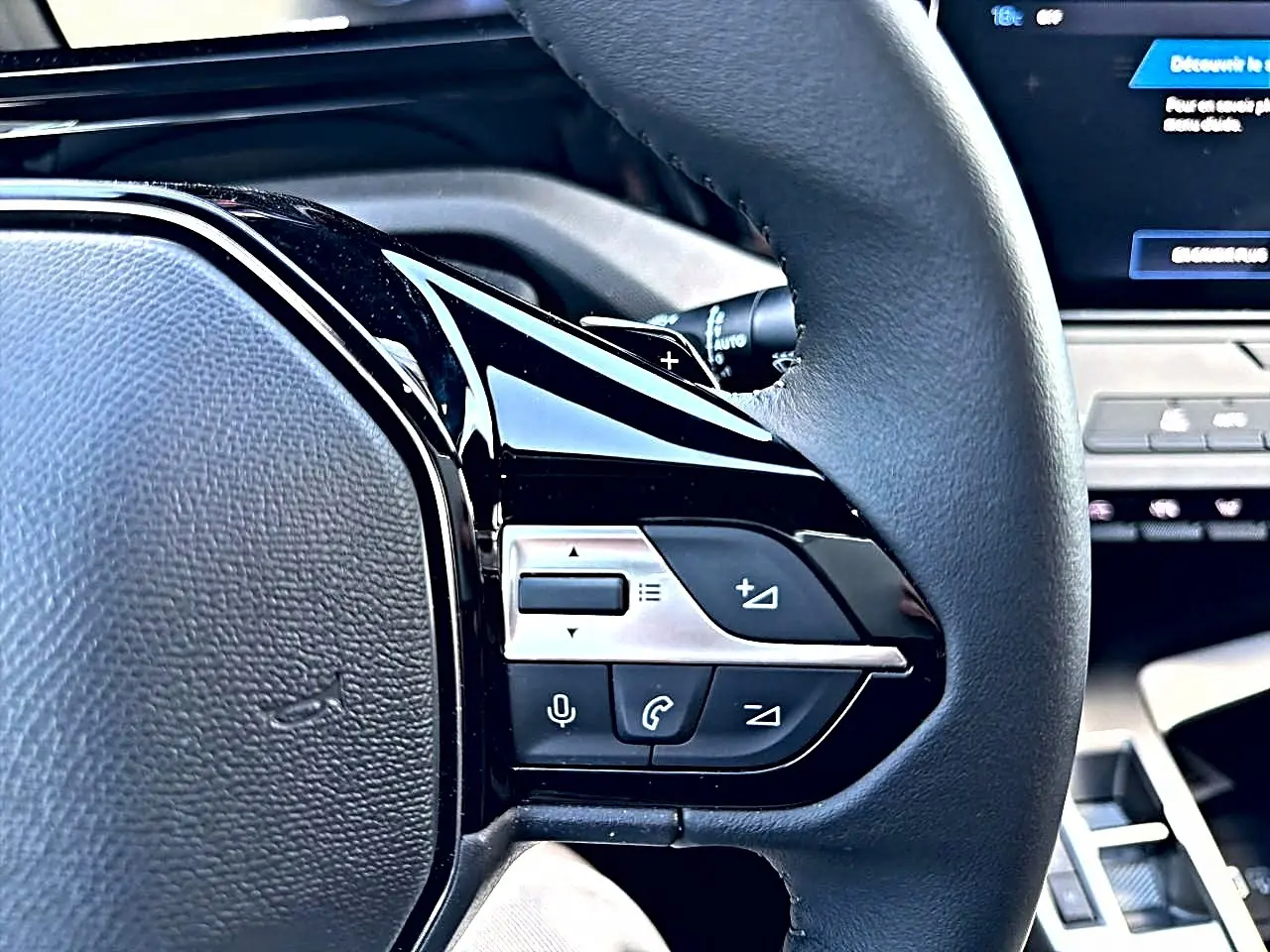 Gros plan sur les commandes multifonctions côté gauche du volant noir du Peugeot 308 gris selenium, avec écran tactile en arrière-plan.
