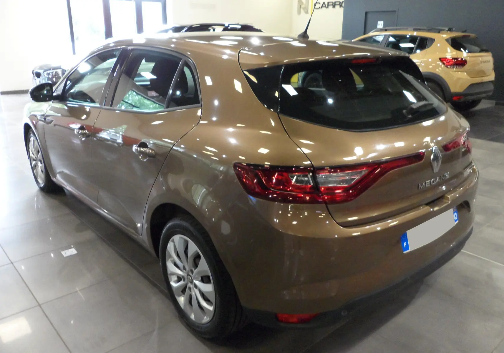 Renault Mégane IV brun capuccino vue 3/4 arrière droit, avec jantes alliage et feux arrière allumés.