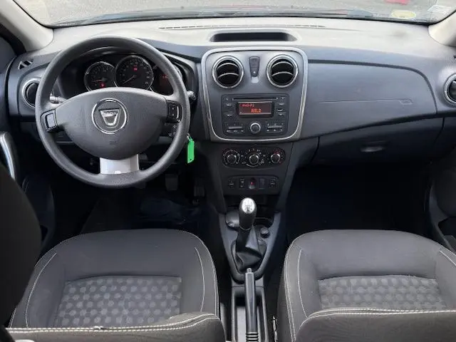 Vue intérieure avant du tableau de bord et volant noir d'une Dacia Sandero 1.5 DCI Laureate avec sellerie tissu gris et console centrale compacte.