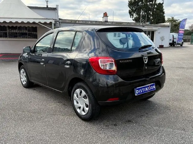 Vue 3/4 arrière d'une Dacia Sandero noire 5 portes, avec feux arrière et logo visibles sur un parking extérieur.