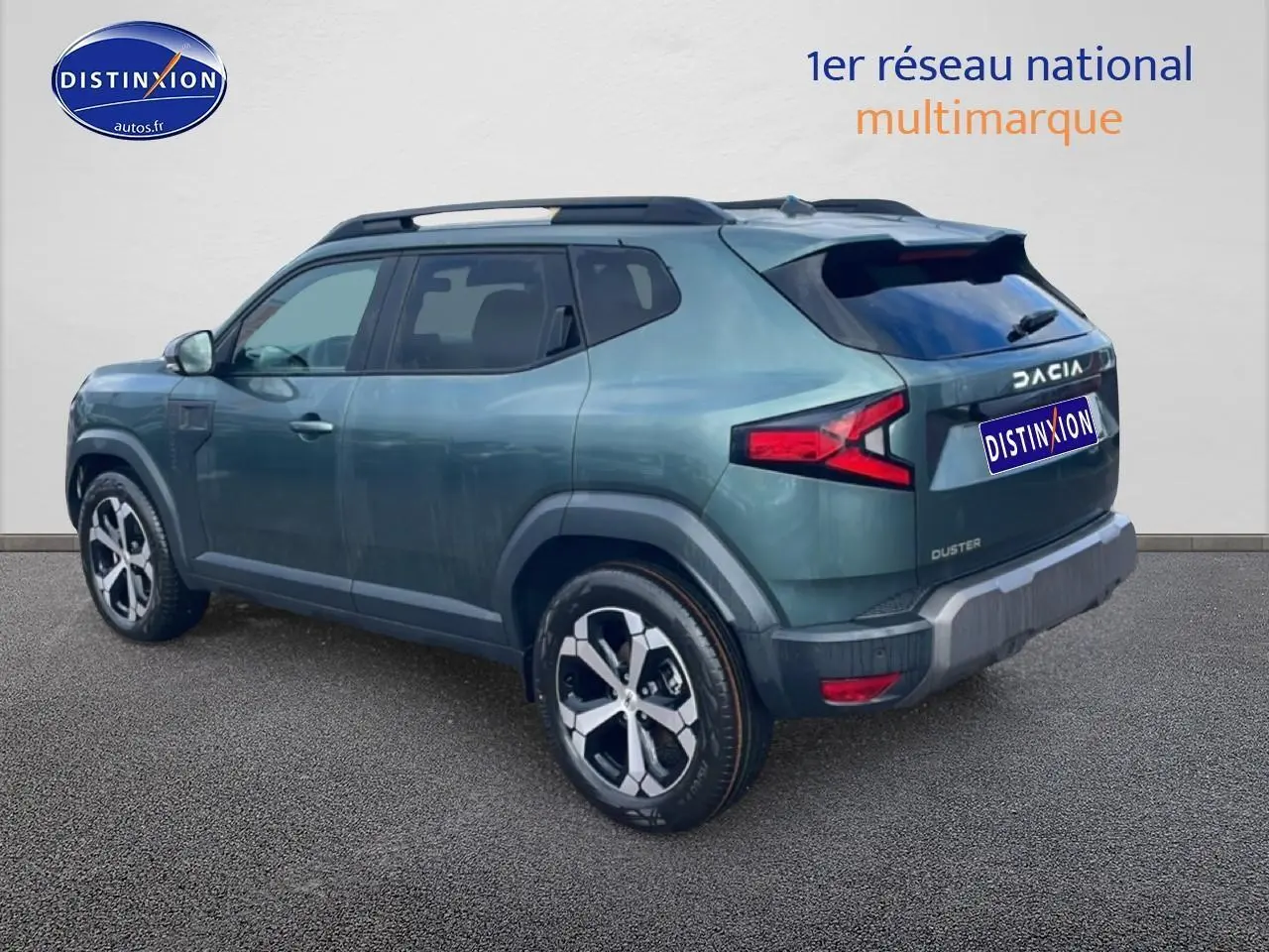 Vue 3/4 arrière droite d'un Dacia Duster vert cèdre avec barres de toit et jantes alu modernes.