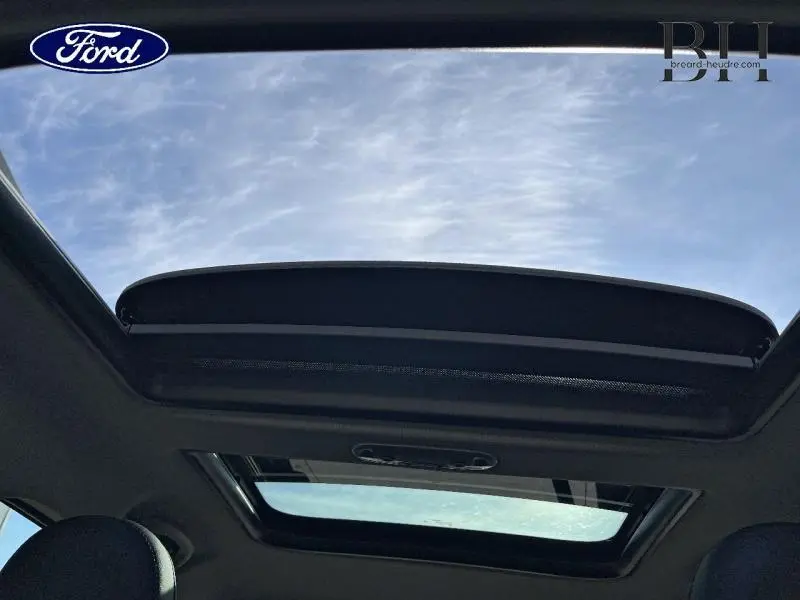 Vue intérieure du toit ouvrant panoramique ouvert du MINI Countryman Cooper SE Moonwalk Grey, laissant voir le ciel bleu.