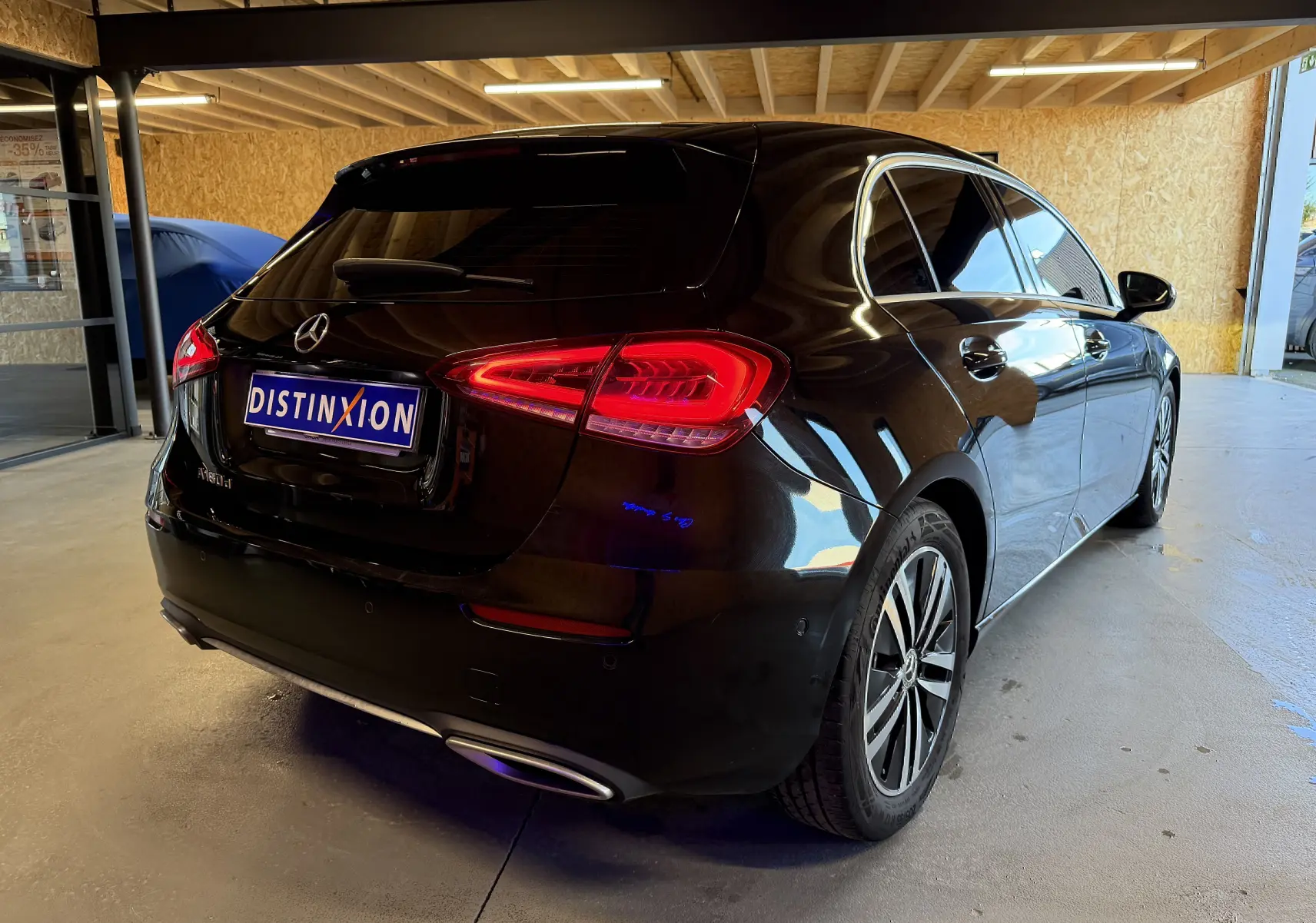 Vue 3/4 arrière droite d'une Mercedes Classe A noire avec jantes alu et sorties d'échappement chromées en intérieur garage.