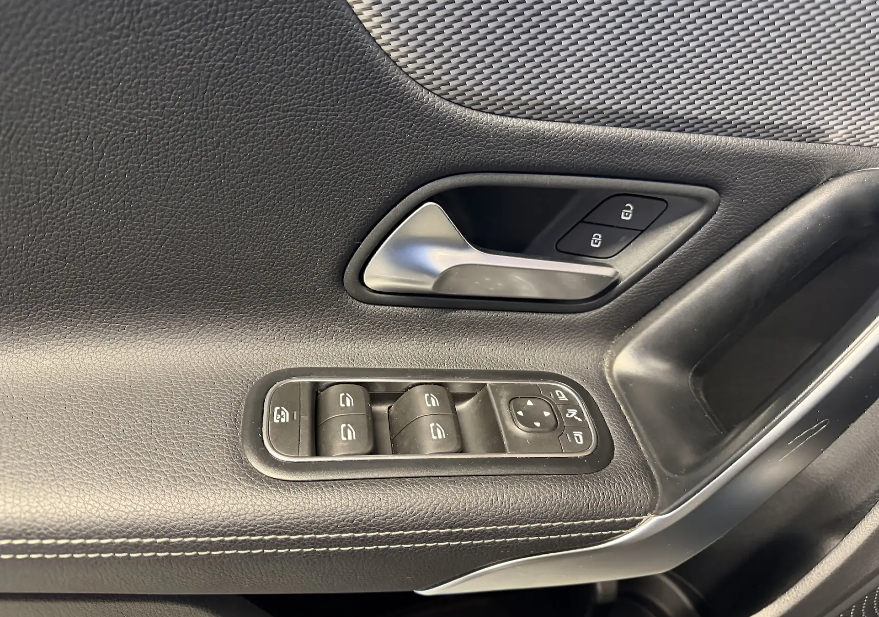 Gros plan sur la garniture intérieure noire côté gauche avec commandes des vitres et poignée de porte chromée.