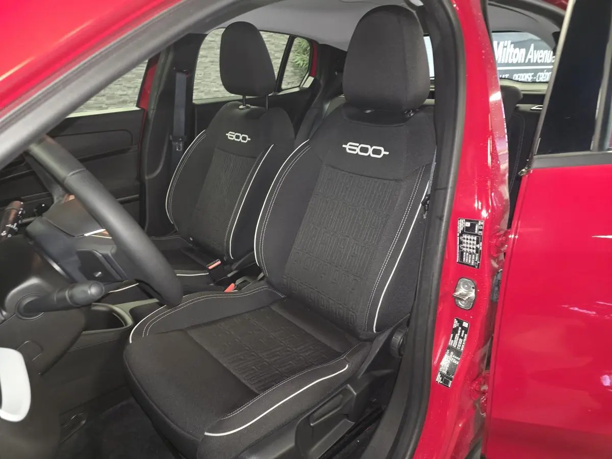 Vue intérieure côté conducteur d'une FIAT 600 rouge 2024, sièges tissu noir avec logo "600" brodé.