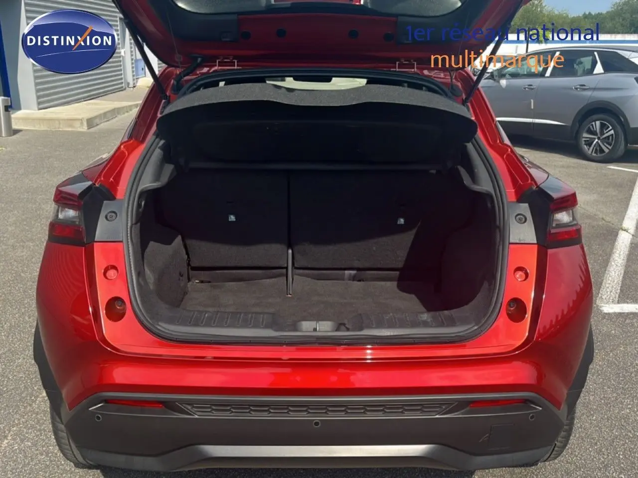 Vue arrière du Nissan Juke rouge Fuji Metal 2024 avec coffre ouvert montrant l'espace de chargement vide.