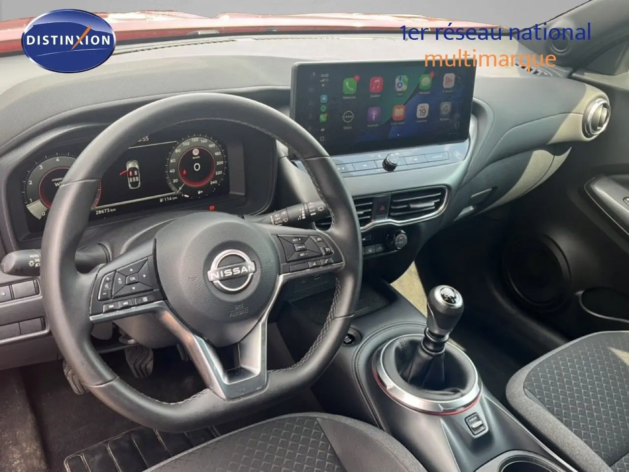Vue intérieure du poste de conduite du Nissan Juke rouge Fuji Metal 2024, avec volant cuir et levier de vitesse manuel.
