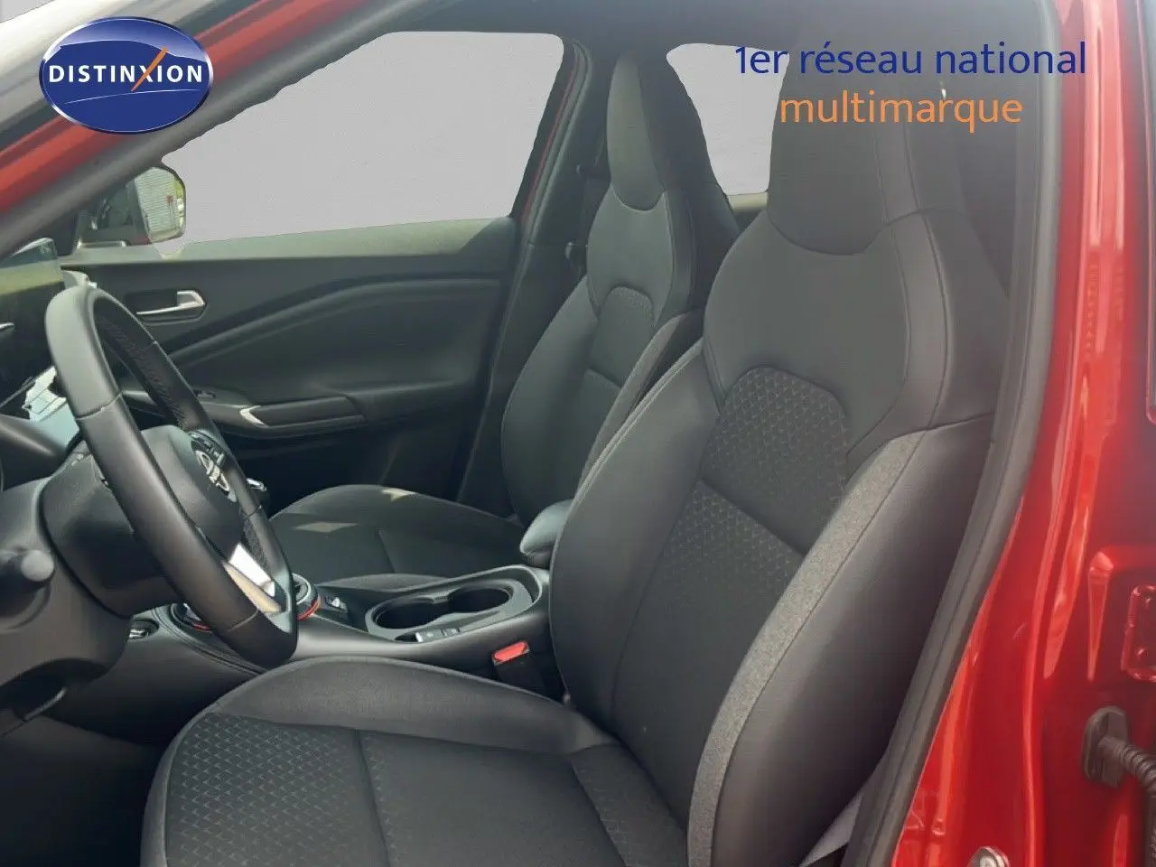 Vue intérieure côté conducteur du Nissan Juke rouge Fuji Metal 2024, montrant les sièges noirs et le volant multifonction.