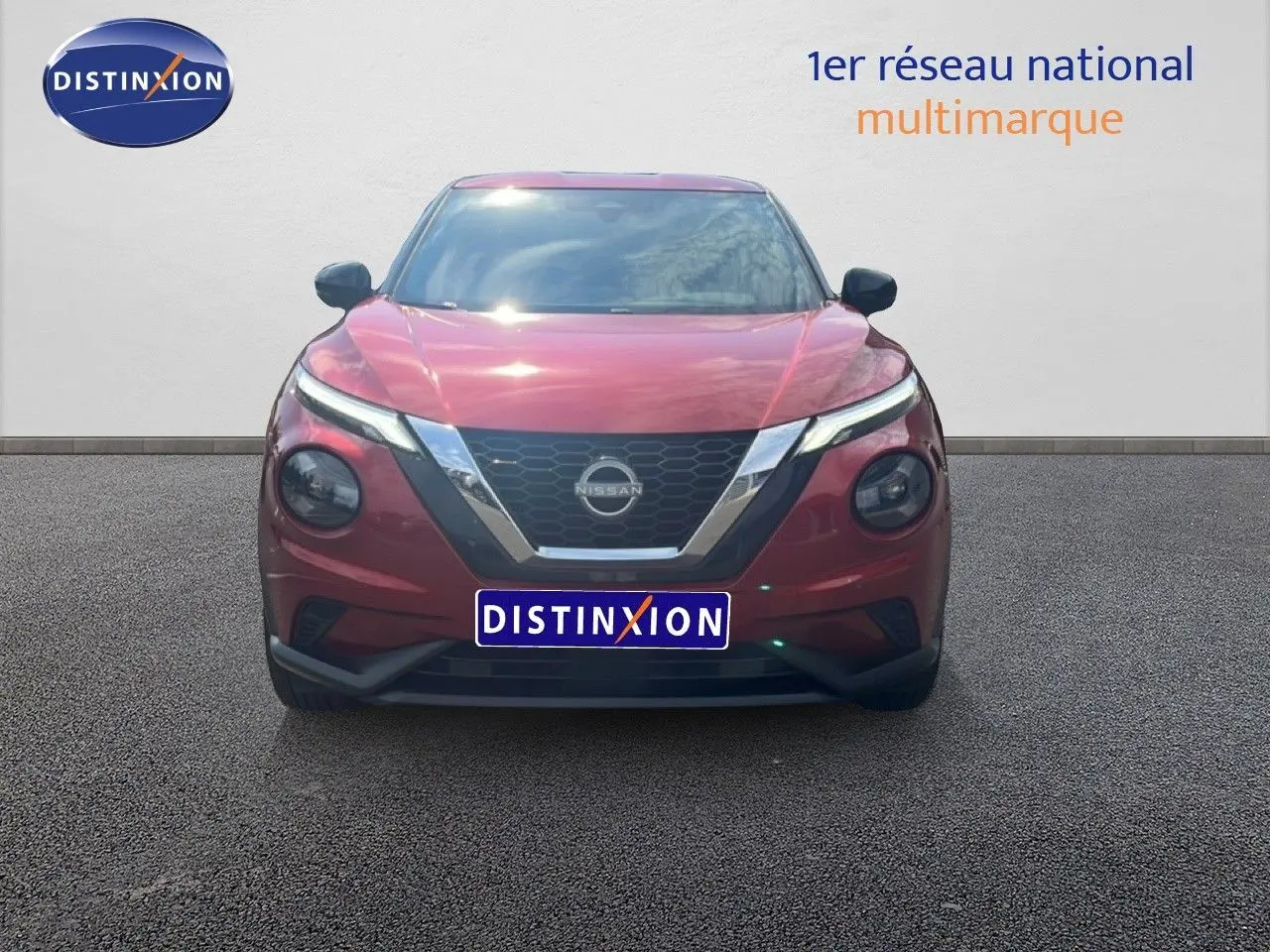 Vue frontale d'un Nissan Juke 2024 rouge Fuji Metal avec calandre en V chromée et phares ronds distinctifs.