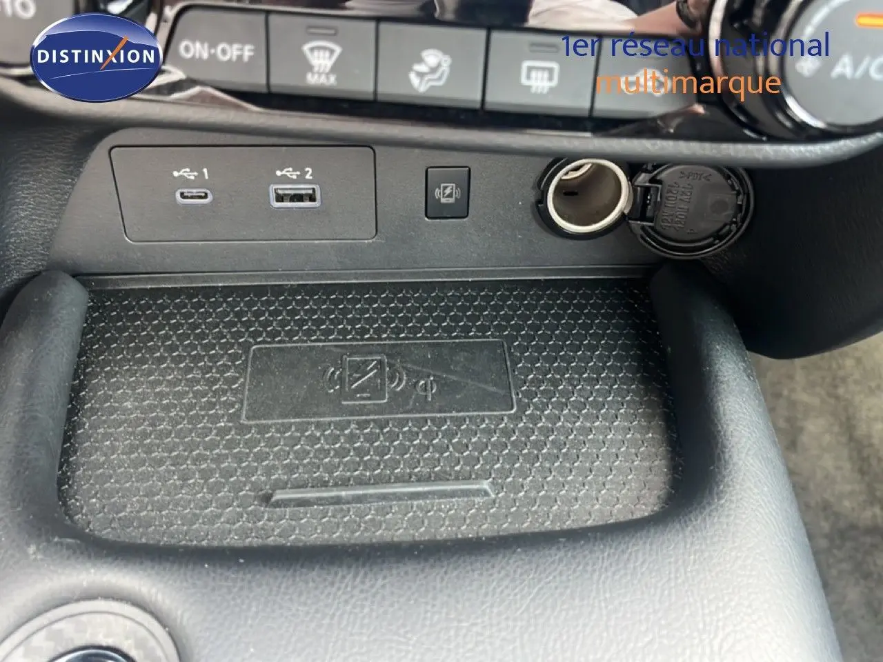 Gros plan sur la console centrale du Nissan Juke rouge Fuji Metal 2024, montrant ports USB, prise 12V et zone de recharge sans fil.