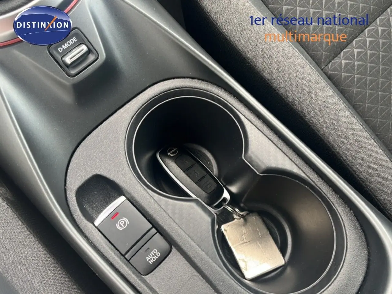 Gros plan sur la console centrale du Nissan Juke rouge Fuji Metal 2024 avec clé dans porte-gobelets et bouton frein à main.
