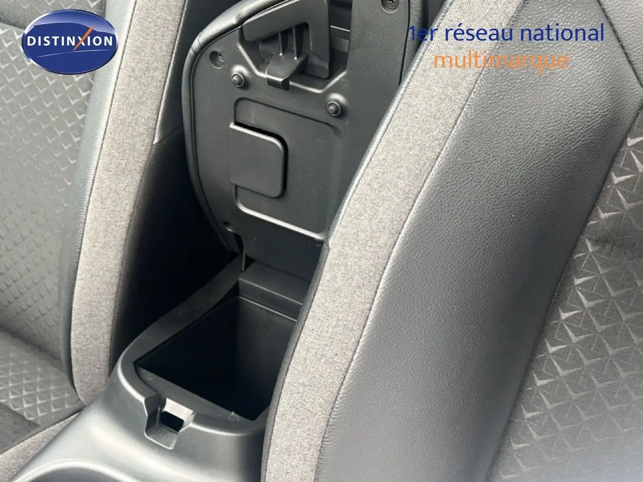 Gros plan sur la console centrale ouverte entre les sièges avant en tissu gris du Nissan Juke 2024.