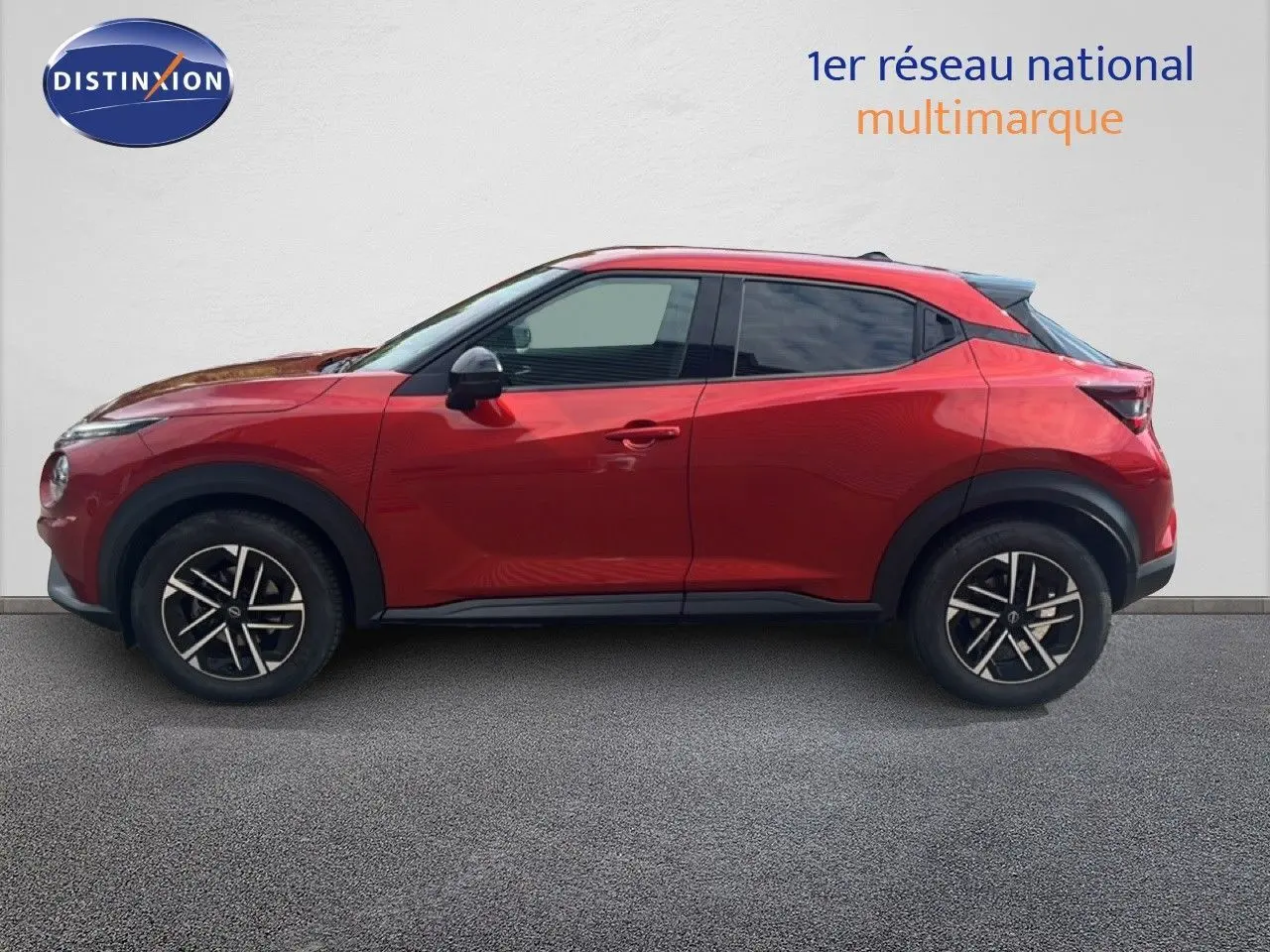 Profil droit d'un Nissan Juke 2024 rouge Fuji Metal avec jantes alliage noires et toit légèrement surélevé.