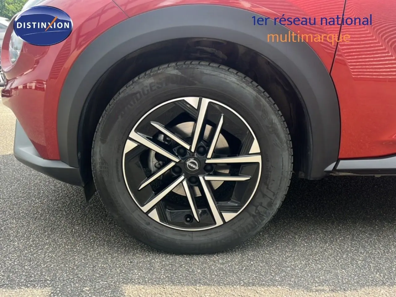 Gros plan sur la roue avant gauche du Nissan Juke rouge Fuji Metal 2024 avec jante alliage noire et argent.