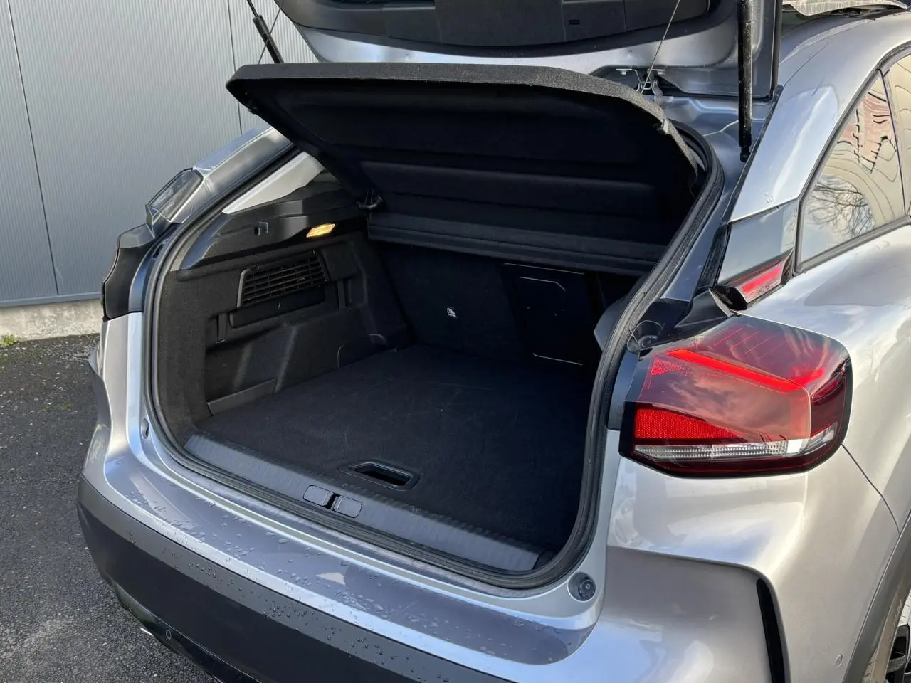 Coffre ouvert vu de l'arrière droit d'une Citroën C4 2024 gris Artense avec feux arrière LED et hayon relevé.