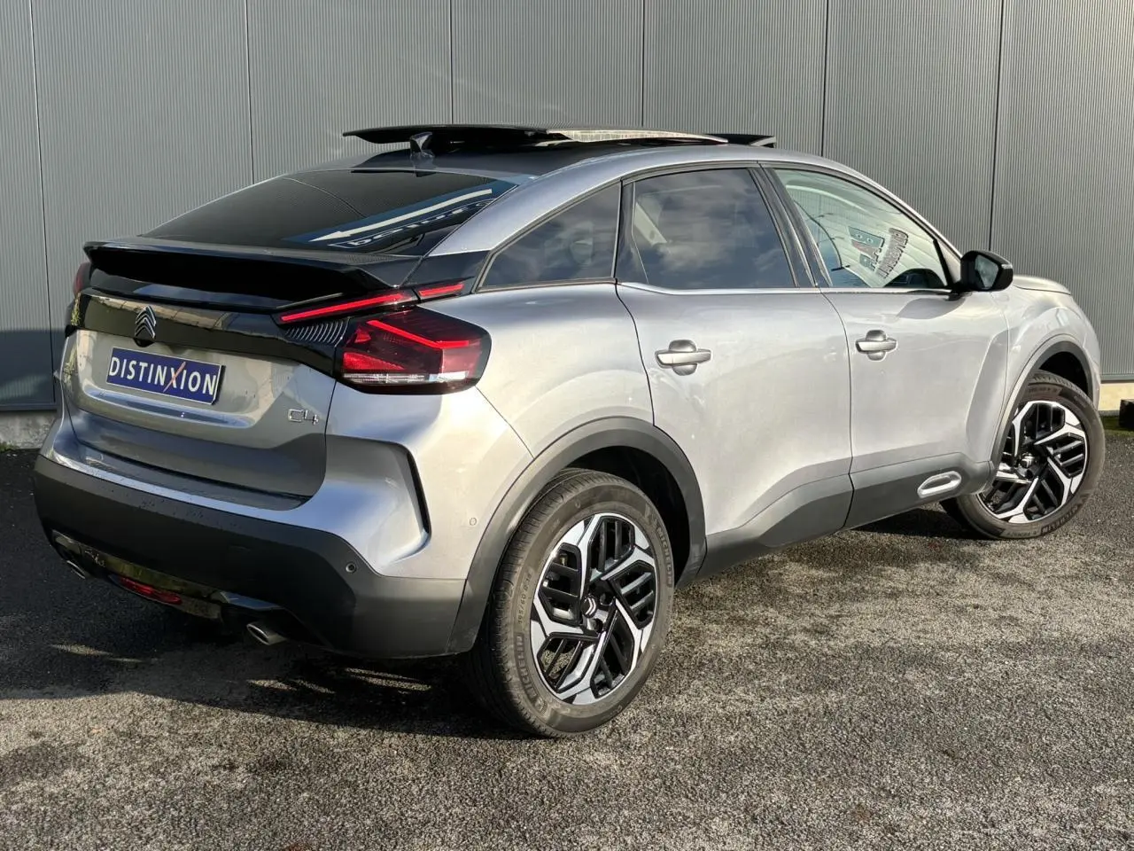 Vue 3/4 arrière droite d'une Citroën C4 gris Artense avec toit ouvrant noir et jantes alliage 18 pouces.