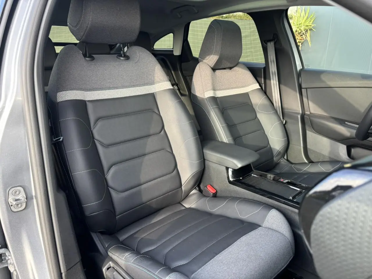 Vue intérieure avant des sièges gris et noirs de la Citroën C4 2024 avec accoudoir central et garniture tissu et cuir.