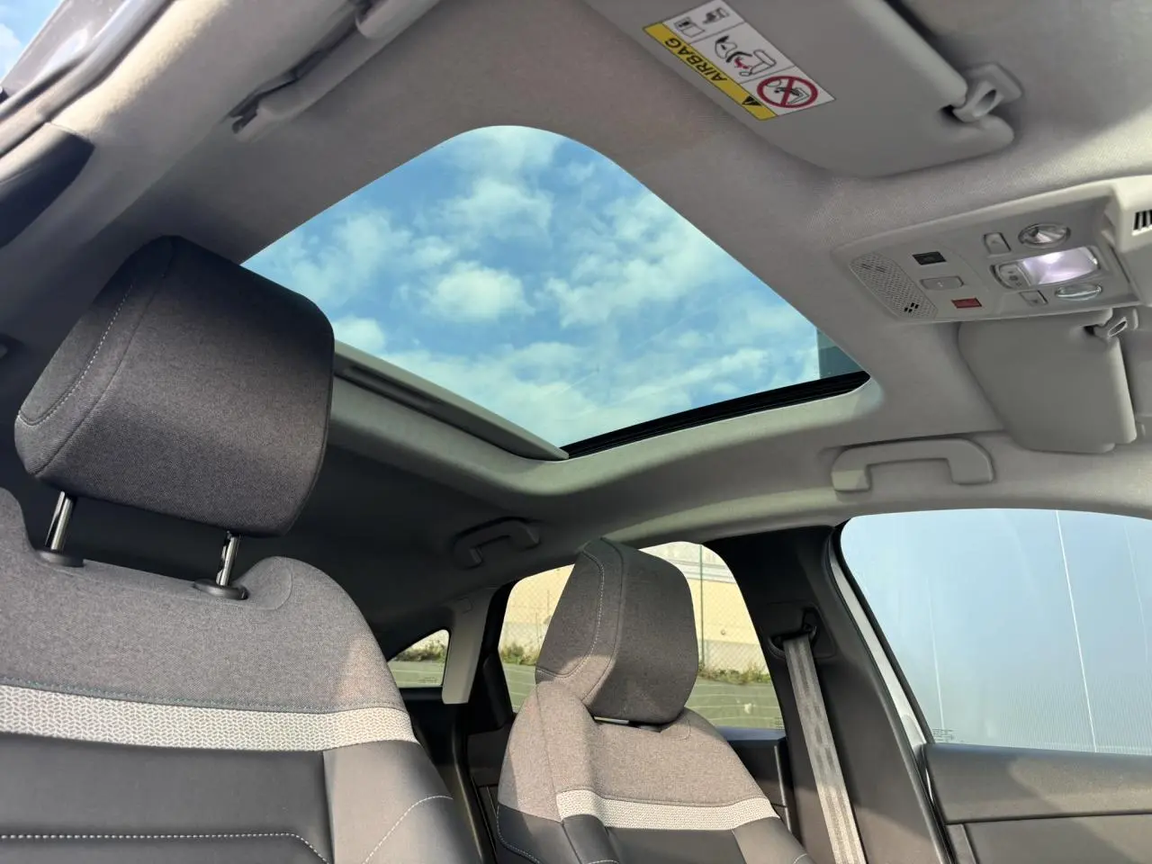 Vue intérieure avant droite de la Citroën C4 2024 avec toit ouvrant électrique et sièges tissu gris chiné.