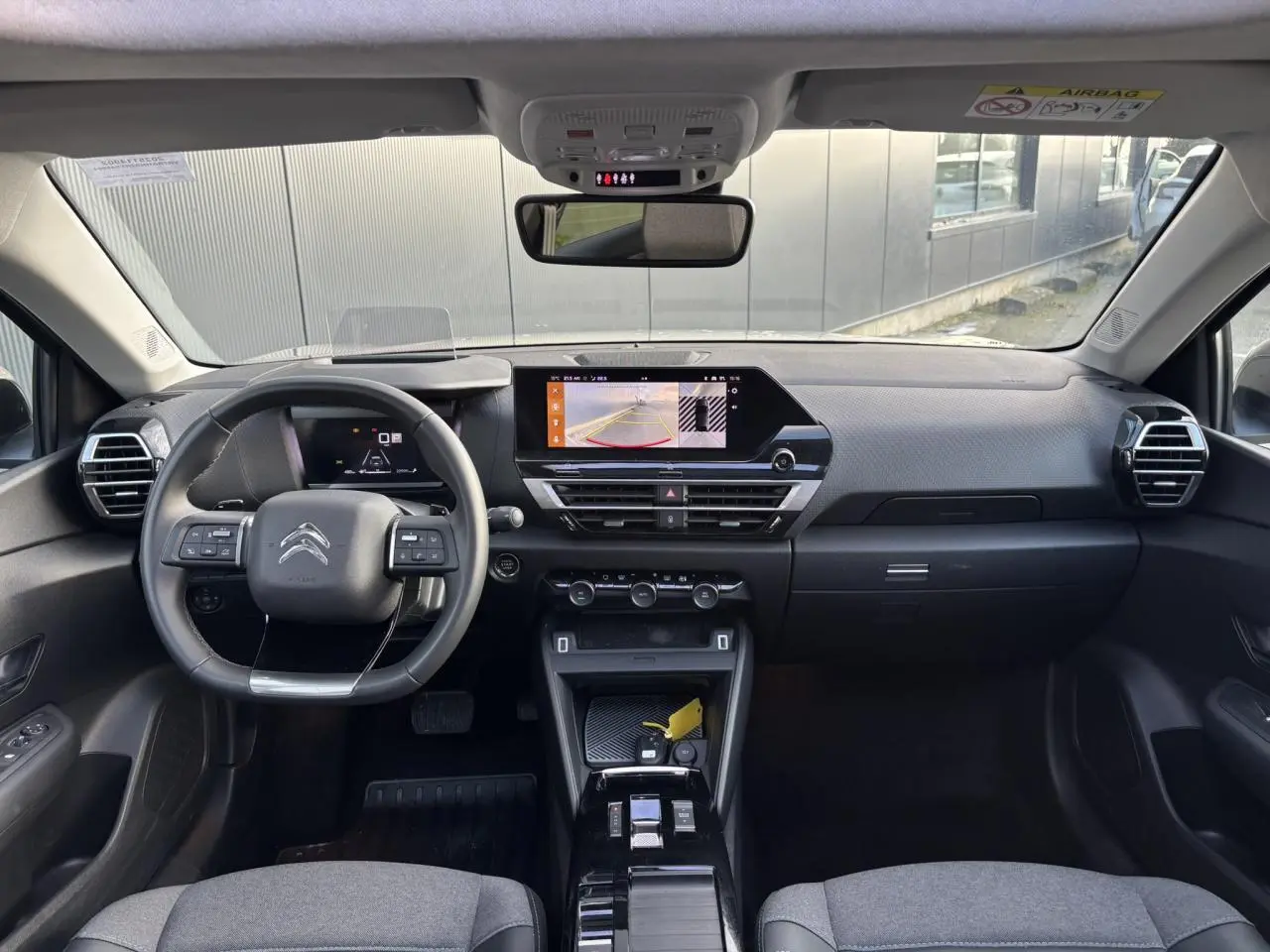Vue intérieure avant de la Citroën C4 2024 avec tableau de bord gris, écran tactile affichant la caméra de recul et volant cuir noir.