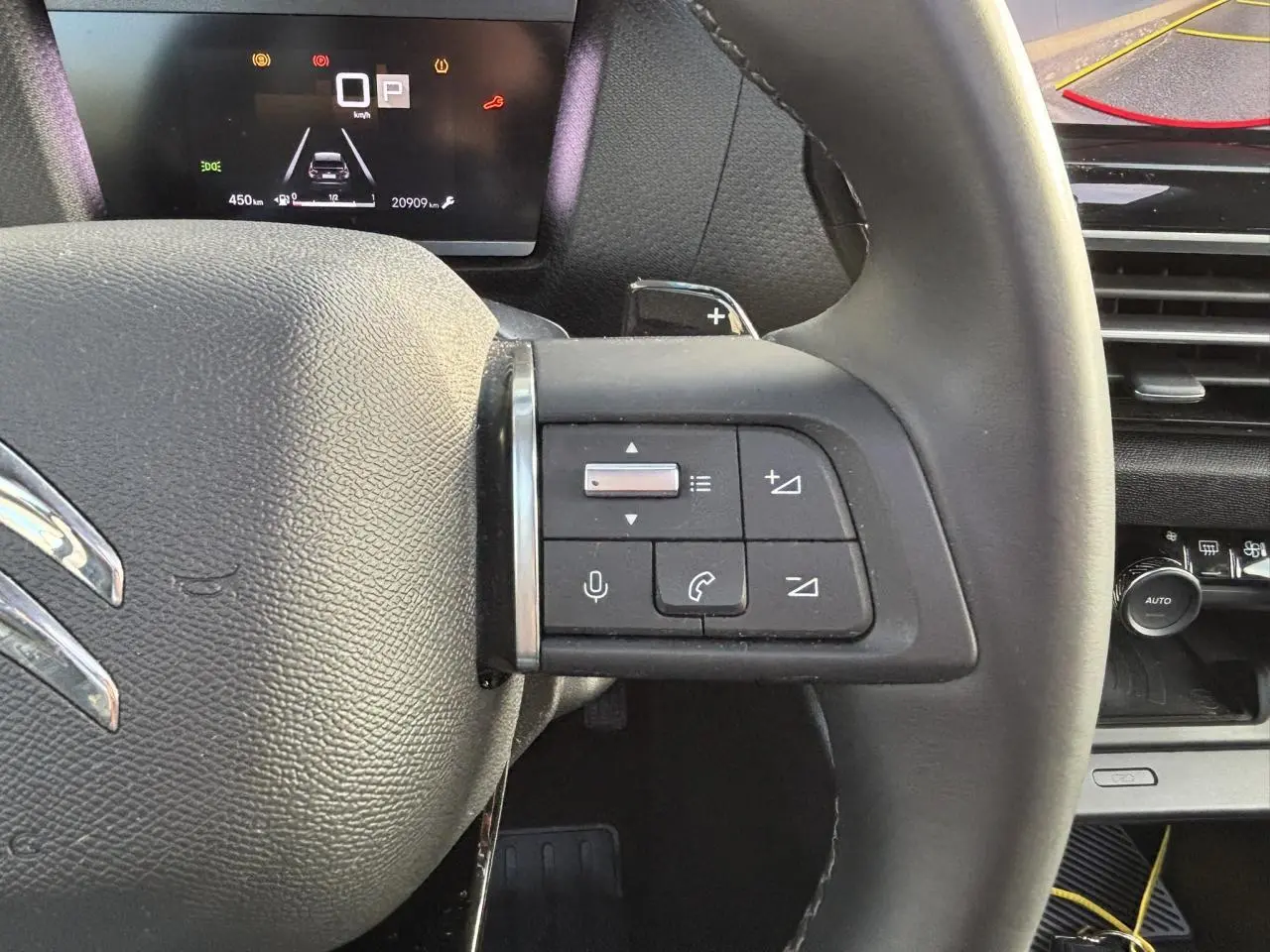 Gros plan sur le volant cuir de la Citroën C4 2024 avec commandes audio et combiné numérique en arrière-plan.