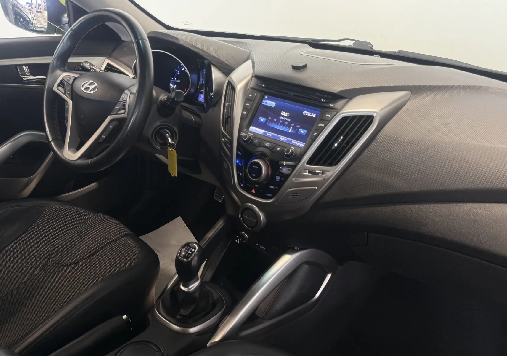 Vue intérieure côté conducteur du Hyundai Veloster 2025, avec tableau de bord noir et levier de vitesses manuel visible.