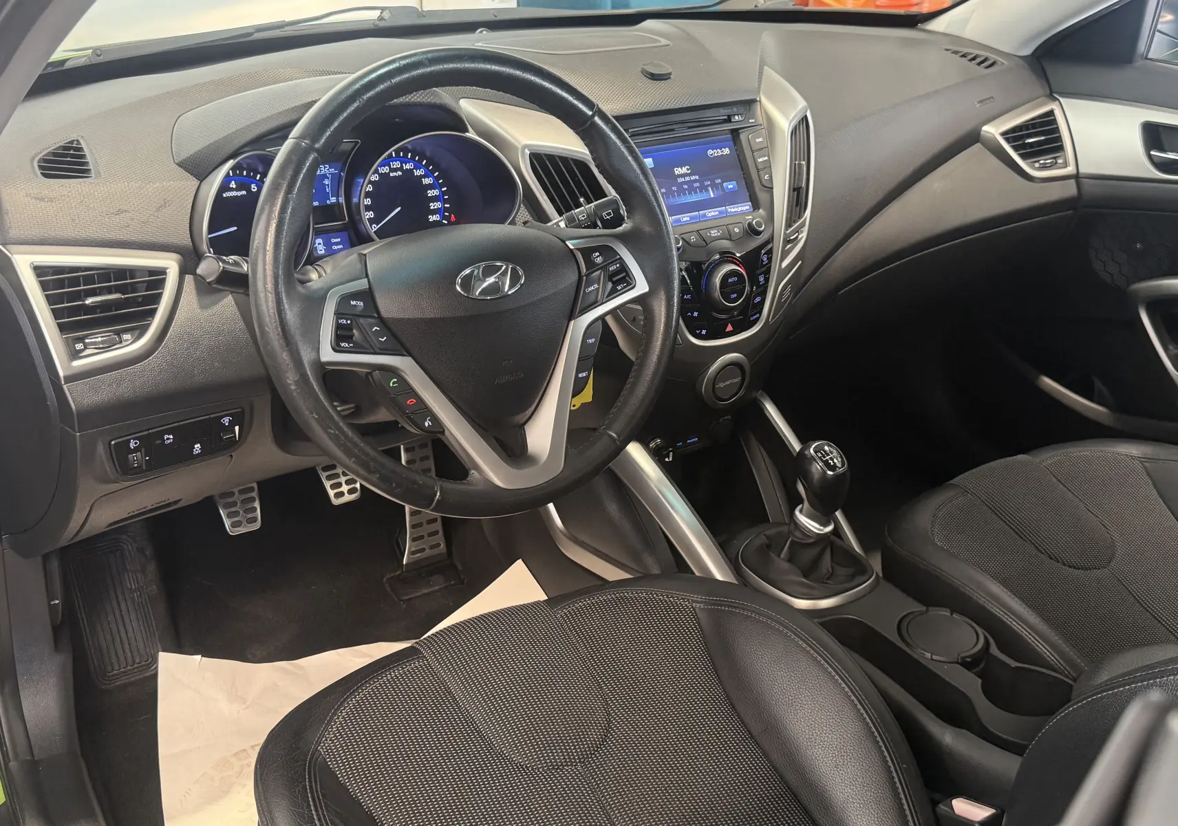 Vue intérieure avant gauche du Hyundai Veloster 2025, volant multifonction et levier de vitesse manuel visibles.