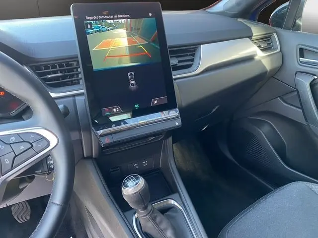 Vue intérieure du tableau de bord du Renault Captur bleuiron, avec écran tactile affichant la caméra de recul et levier de vitesse manuel.