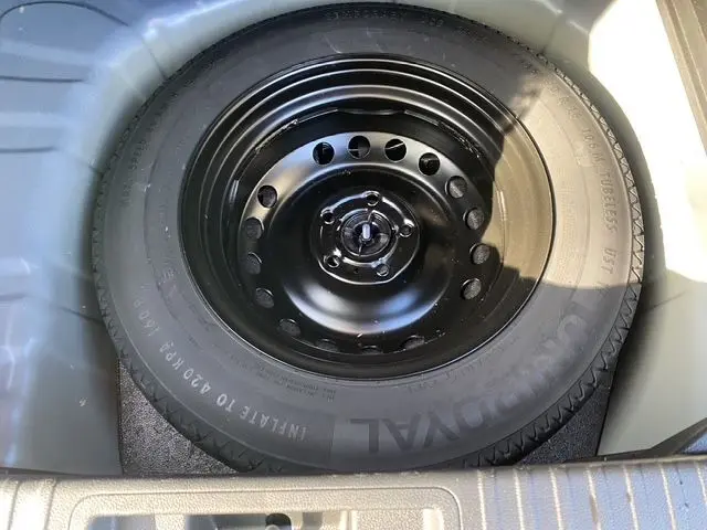 Gros plan sur la roue de secours noire du coffre du Renault Captur TCe 90 Evolution 2024, peinture bi-ton bleuiron et toit noir.