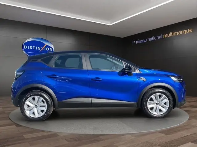 Vue de profil côté gauche du Renault Captur TCe 90 Evolution bleu iron avec toit noir, roues 17'' Nymphea en intérieur showroom.