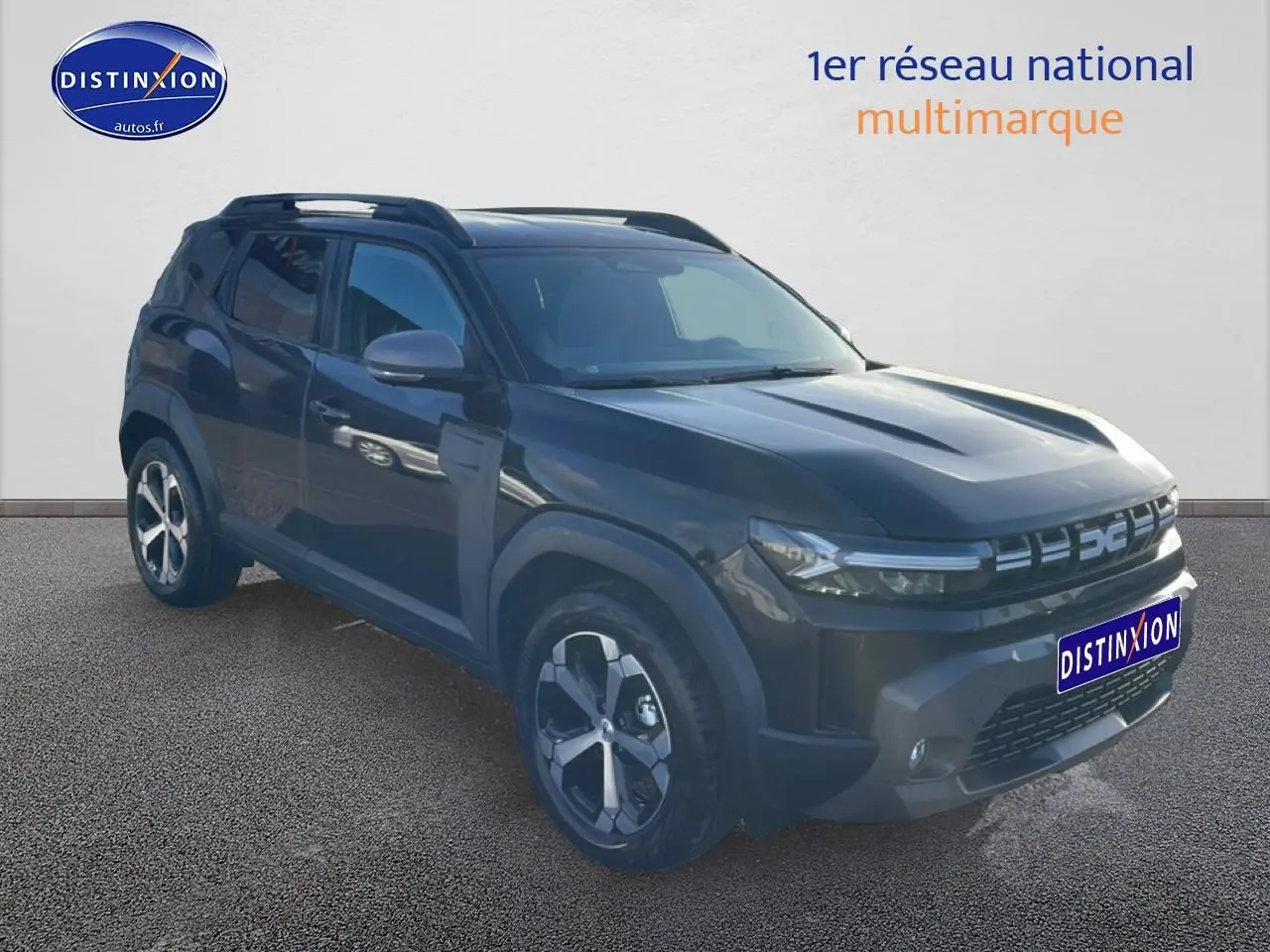 Dacia Duster noir 3/4 avant droit, jantes alu, barres de toit et calandre moderne avec logo lumineux.