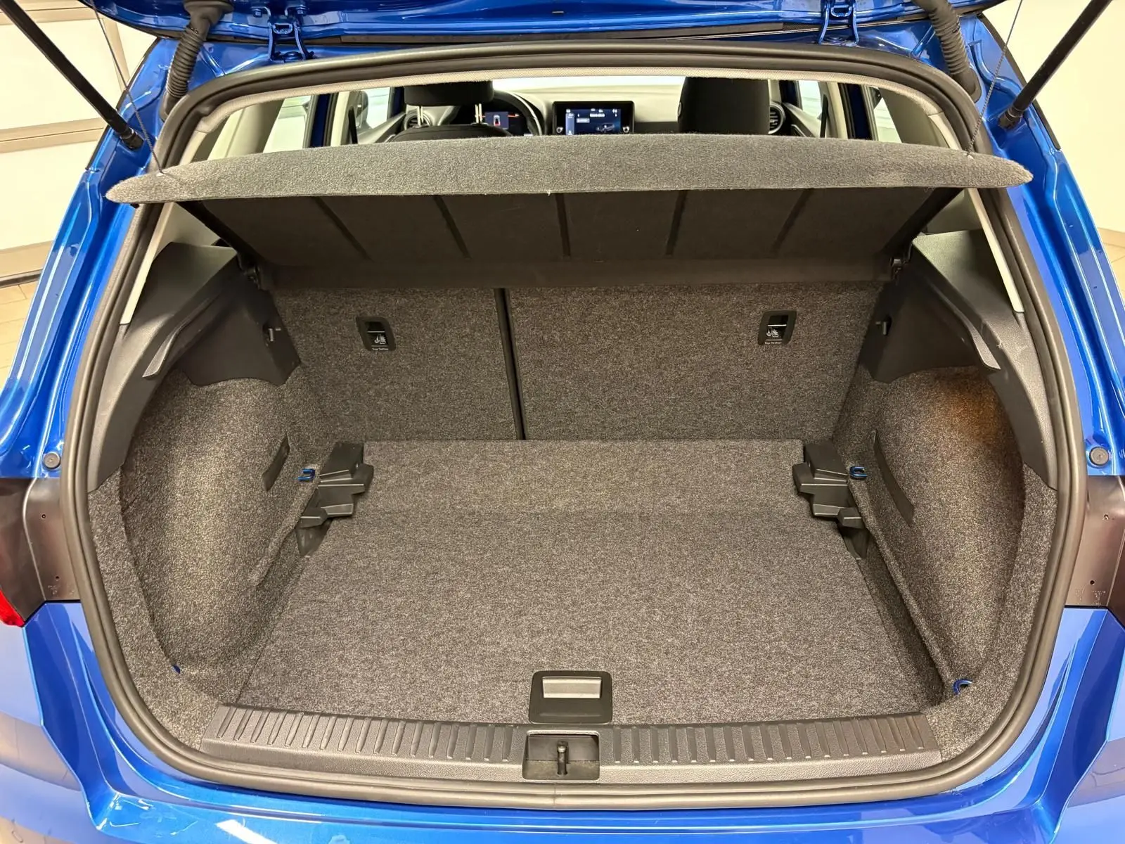 Coffre ouvert vu de l'arrière d'un SEAT Arona 2025 bleu saphir avec intérieur de coffre gris et toit noir visible.