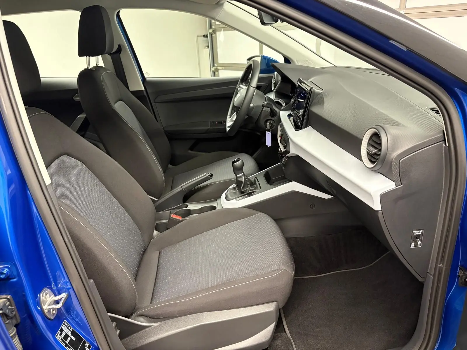 Vue intérieure côté conducteur du SEAT Arona bleu saphir, montrant les sièges tissu et la console centrale avec boîte manuelle.