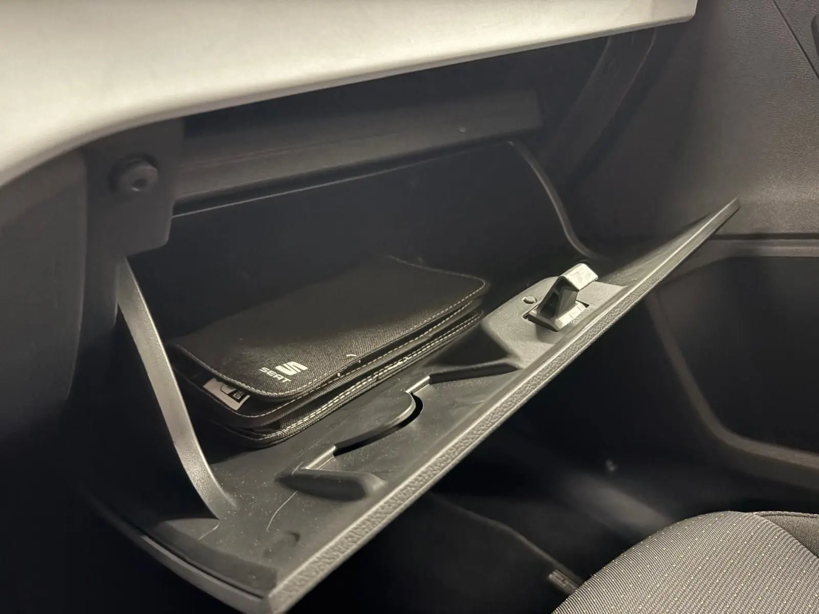 Gant de boîte à gants ouvert côté passager avec pochette noire SEAT visible à l'intérieur, intérieur sombre.