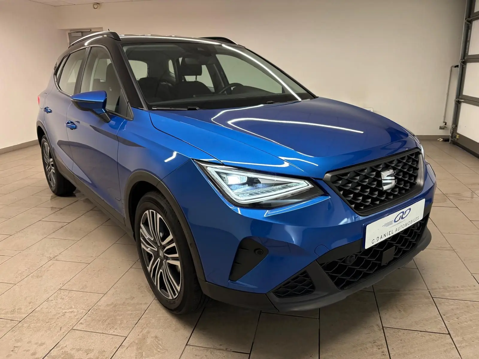 Vue 3/4 avant droite du SEAT Arona 2025 en bleu saphir avec toit noir, mettant en valeur sa calandre et ses phares LED.