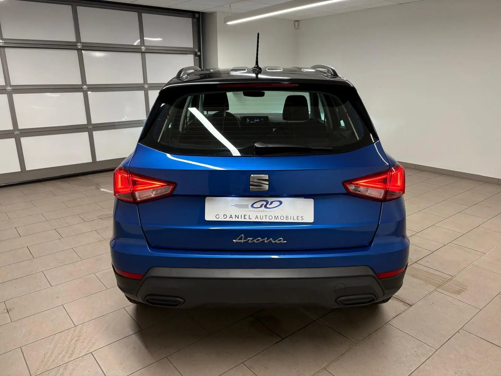 Vue arrière d'un SEAT Arona 2025 bleu saphir avec toit noir, dans un intérieur neutre et éclairé.