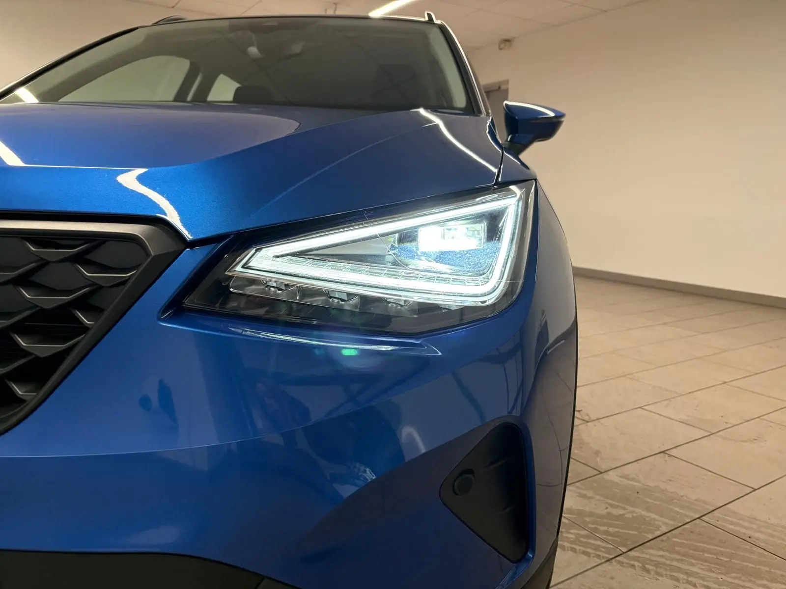 Gros plan sur l'avant droit du SEAT Arona 2025 bleu saphir avec phare LED allumé et calandre noire.