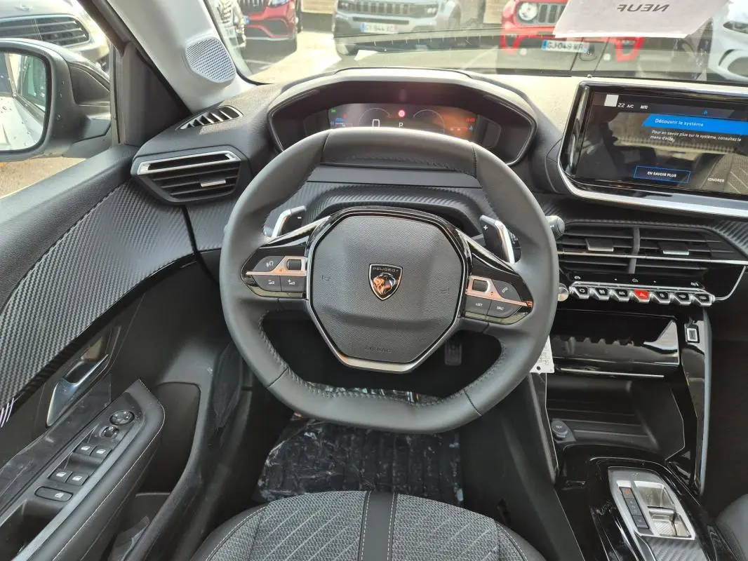 Vue intérieure centrée sur le volant cuir noir et le cockpit numérique de la Peugeot 208 Hybrid 110 Allure 2025.