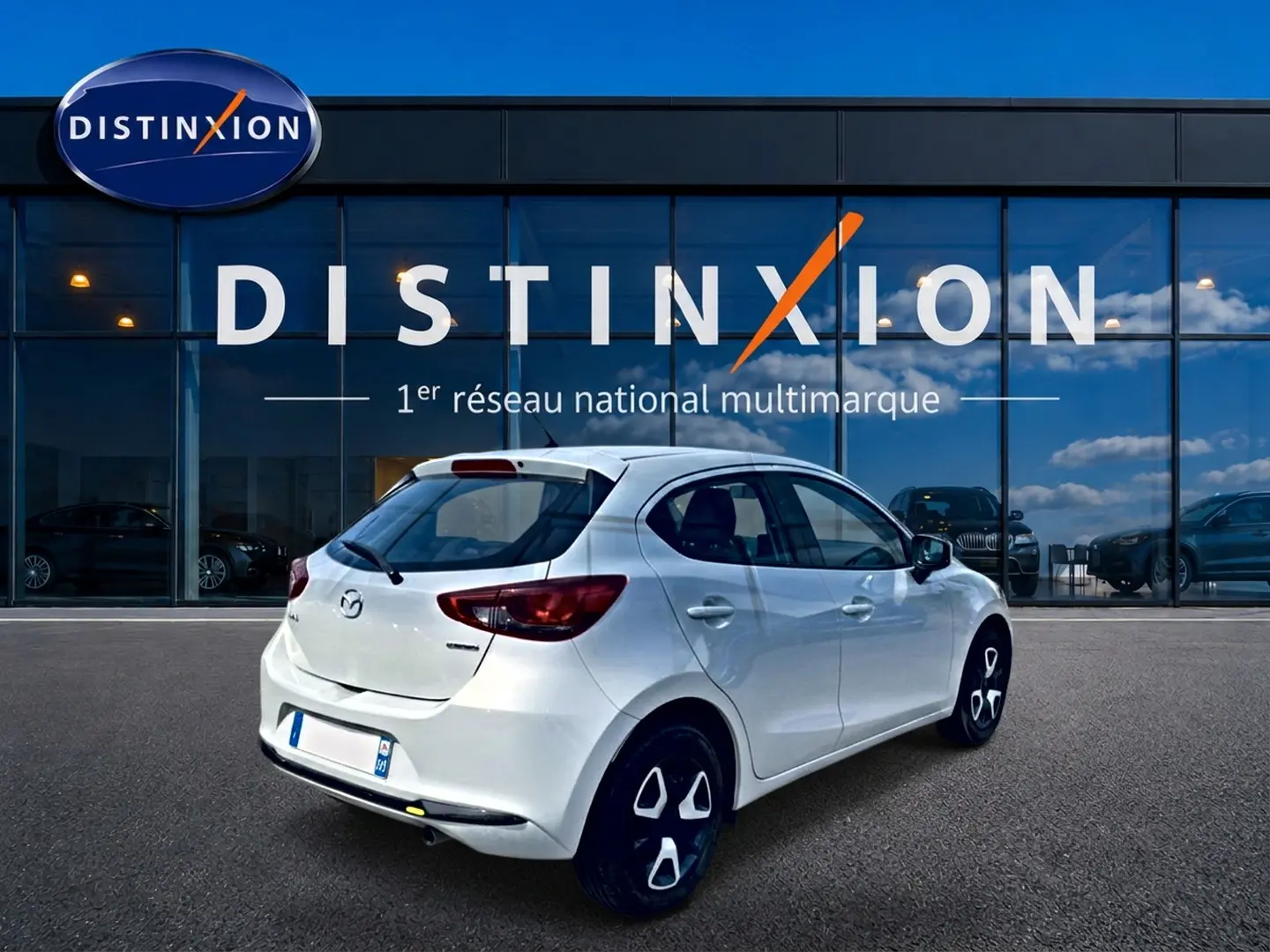 Vue 3/4 arrière droite d'une Mazda2 blanche 2024 stationnée devant une vitrine Distinxion.