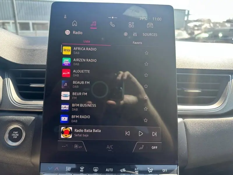 Vue intérieure centrée sur l'écran tactile multimédia du Renault Captur 2025 avec commandes radio et bouton Start Engine Stop visible.