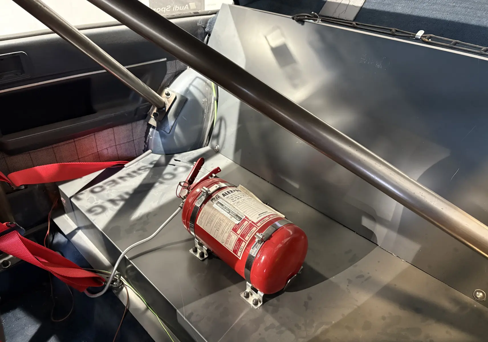 Gros plan sur l’étiquette FIA d’un siège baquet rouge de compétition dans un Audi Coupé GT noir de 1983.